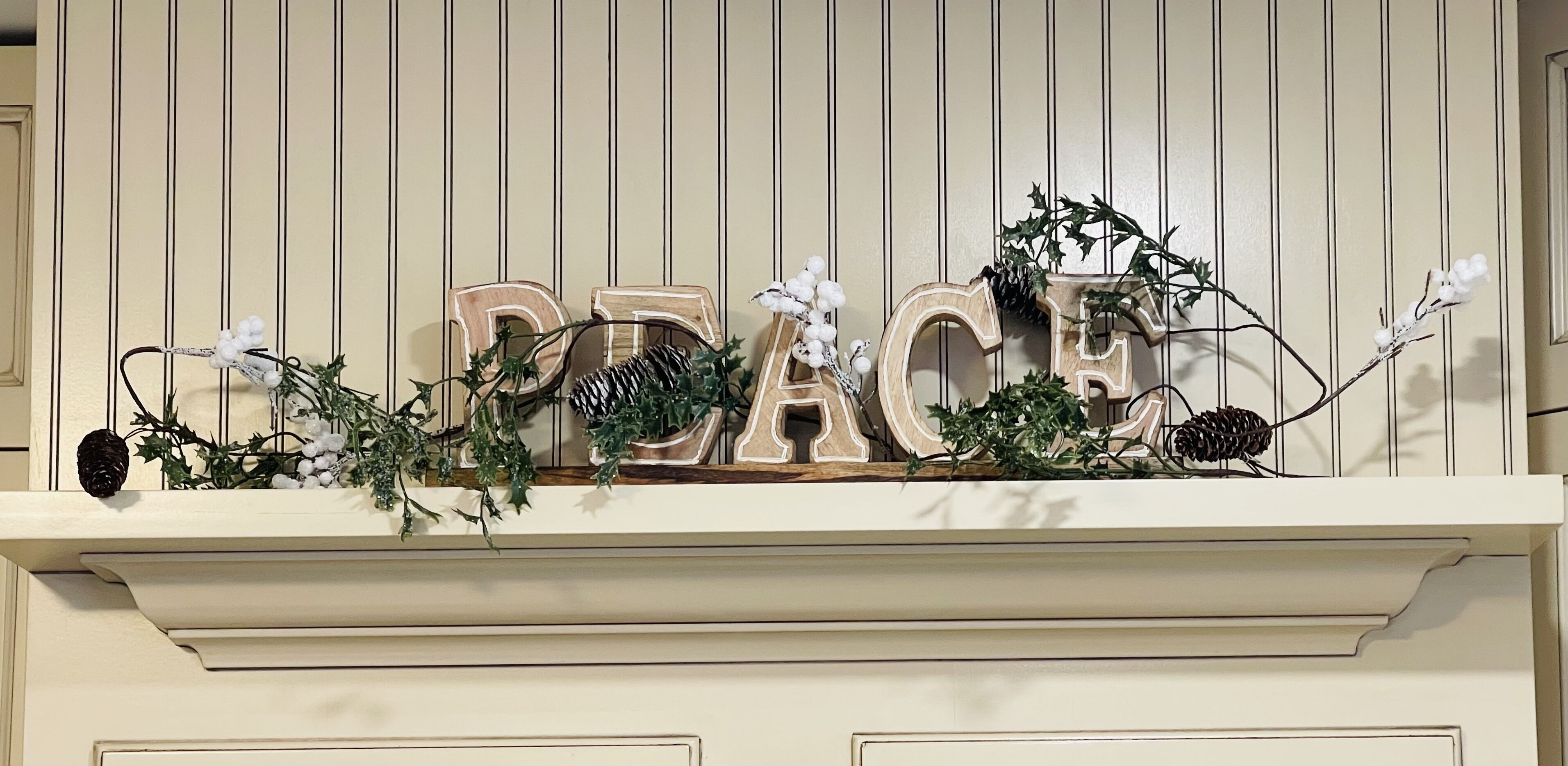 A decorative sign with the word "PEACE" spelled out in wooden letters, adorned with greenery and pinecones.
