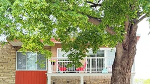 A two-story townhouse with a front porch, a small balcony, and a tree in front.