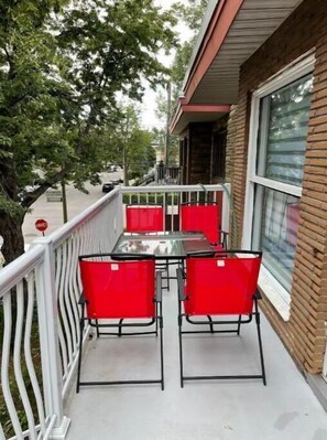 A balcony with a table and four red chairs, a white railing, and a brick building with a window. - Full apartment, quick access with 40 Highway and 15 Highway. Free Parking (Montréal)