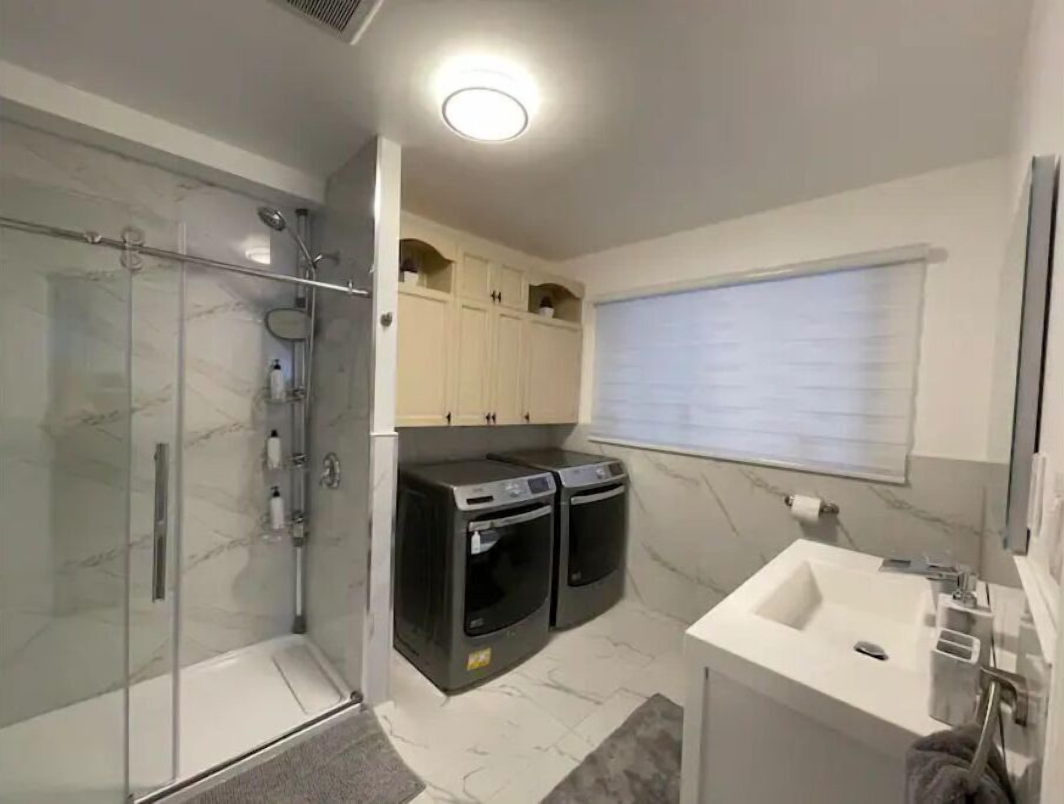 Casa de banho moderna com cabine de duche em vidro, máquina de lavar roupa e secadora integradas e lavatório branco.