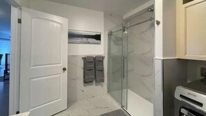 A bathroom with a glass shower, a white door, and a towel rack.