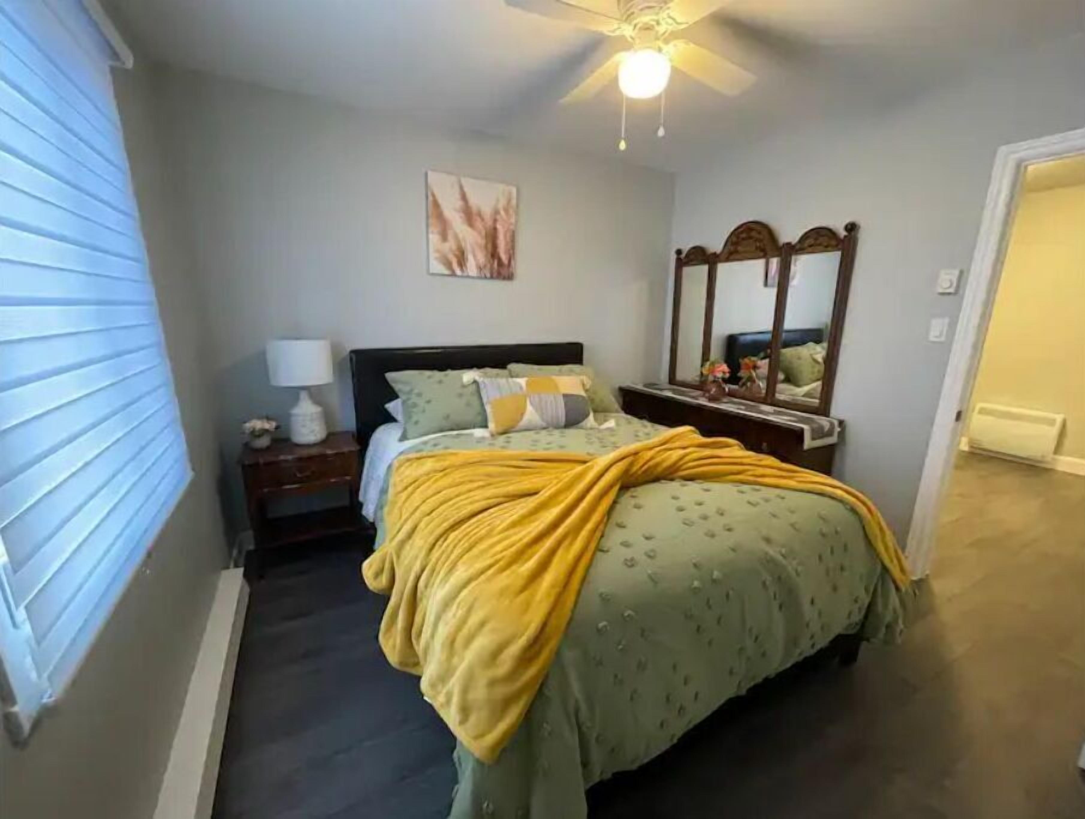 A bedroom with a bed, a nightstand, a lamp, a mirror, and a ceiling fan.