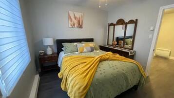 A bedroom with a bed, a nightstand, a lamp, a mirror, and a ceiling fan.