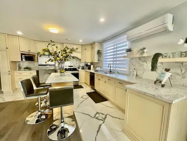 A modern kitchen with white cabinets, a marble countertop, and a central island with chairs. - Full apartment, quick access with 40 Highway and 15 Highway. Free Parking (Montréal)