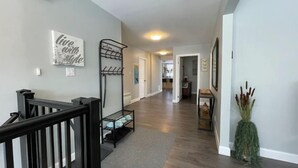 A hallway with a black railing, a coat rack, and a decorative wall piece.