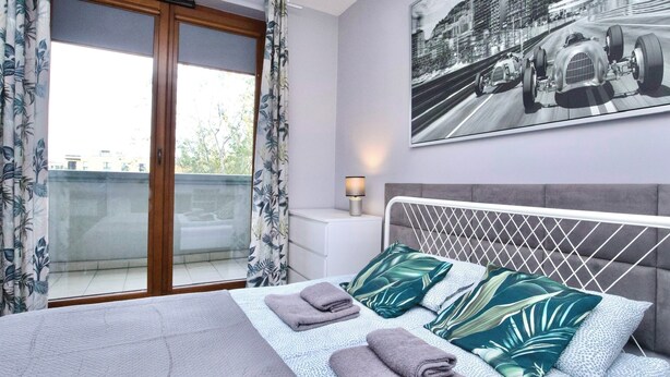 A bedroom with a bed, pillows, a nightstand, a lamp, and a window with curtains.