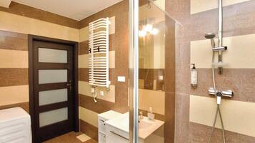 A modern bathroom with a glass shower enclosure, a white sink, and a towel rack.