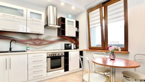 A modern kitchen with white cabinets, a built-in oven, and a dining area with a round table and four chairs.