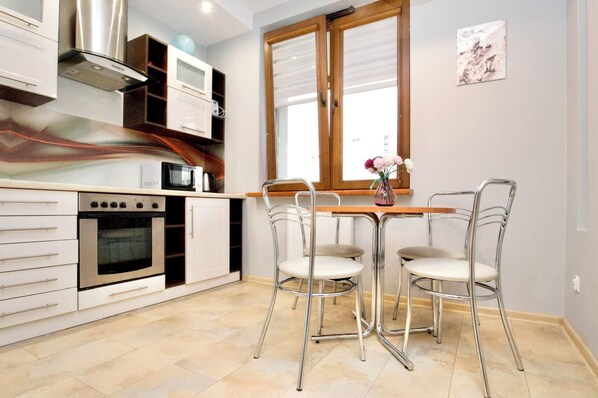 A modern kitchen with white cabinetry, a built-in oven, a microwave, and a dining area with two chairs and a table. - Rodzinny apartament dla 6 osób (Kraków)