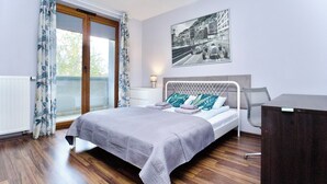 A bedroom with a bed, a desk, a window with curtains, a radiator, and a wall-mounted picture.