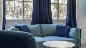 En moderne stue med en grå sofa, et rundt hvidt sofabord og udsigt ud af et vindue med metalgitre.