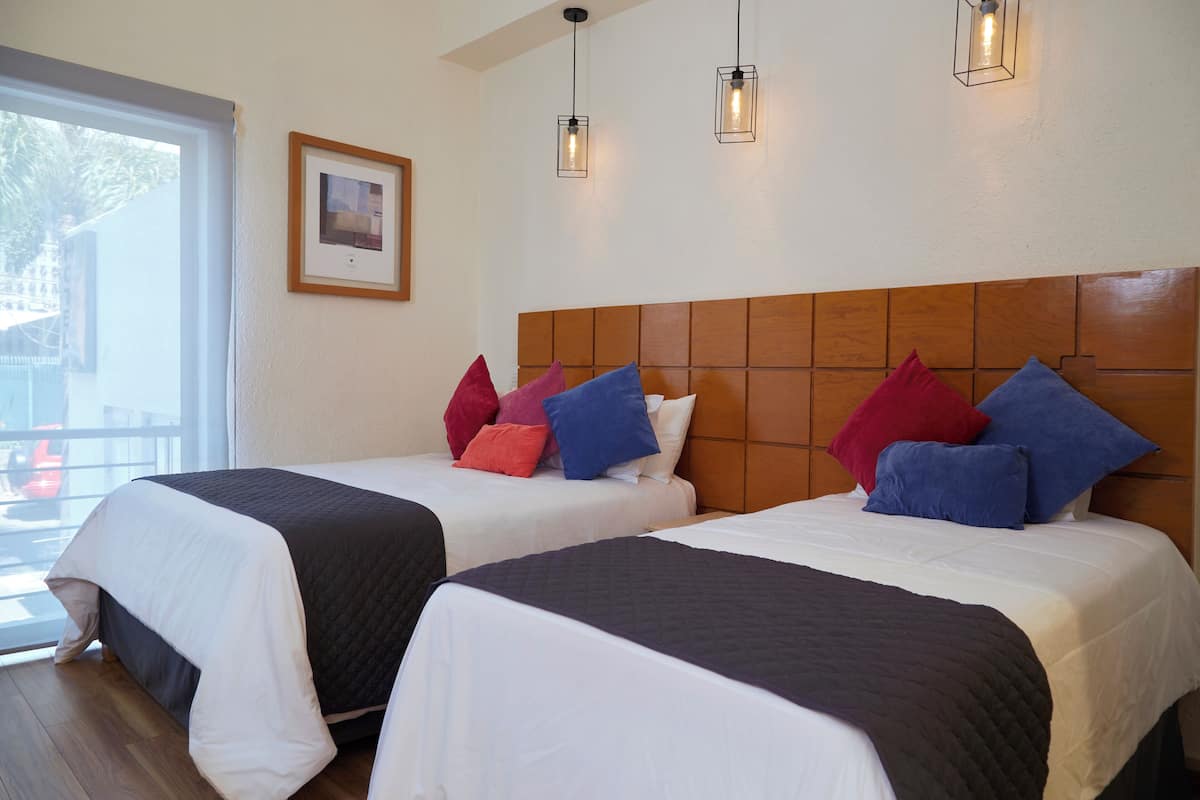 Hotellihuone, jossa on kaksi sänkyä, suuri ikkuna ja seinällä oleva kehystetty taulu.