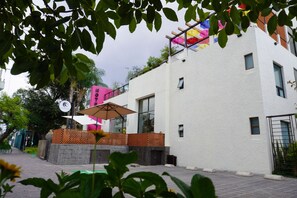 Ein modernes Gebäude mit weißer Fassade, einem kleinen Fenster und einem Balkon mit einem bunten Sonnenschirm.