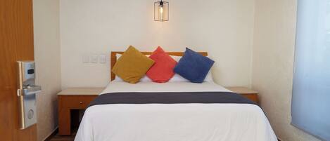 A hotel room with a bed, a bedside table, a nightstand, a wall-mounted light fixture, and a window.