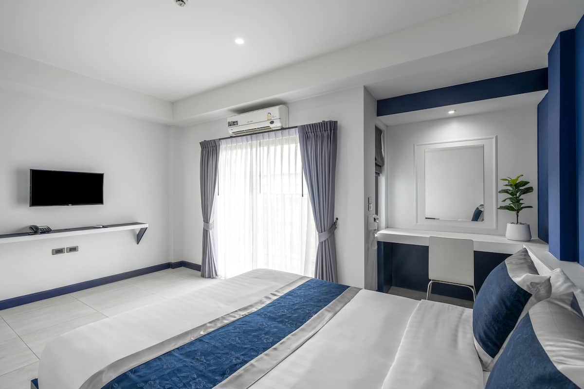Quarto de hotel moderno com uma cama grande, televisão de tela plana na parede, escrivaninha com espelho e uma planta em vaso.