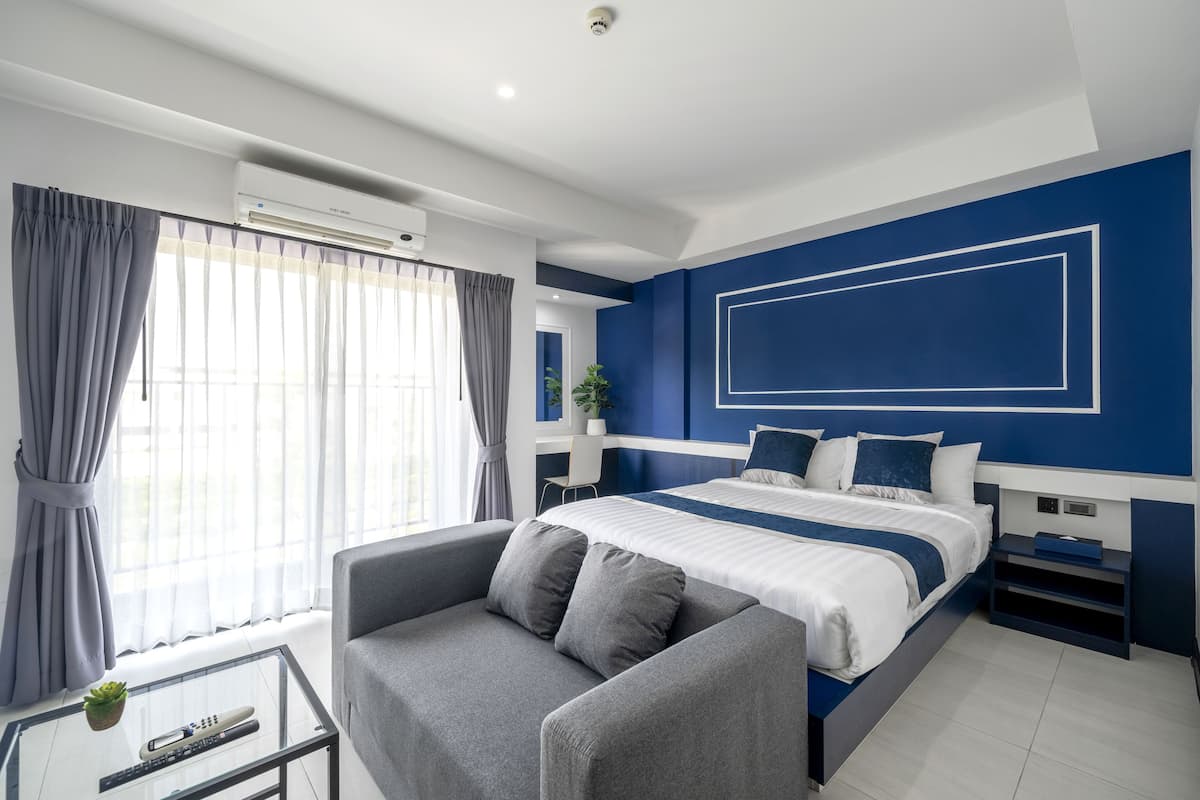 Quarto de hotel moderno com uma cama grande, um sofá, uma mesa de centro de vidro e vista para o exterior.