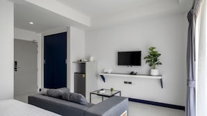 A modern hotel room with a bed, a sofa, a small table, a TV, a plant, and a kitchen area. - The Parc Bangna (Bang Phli)