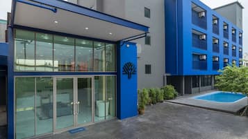 A modern building with a glass entrance, a blue logo, and a small outdoor pool.