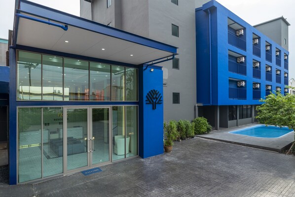A modern building with a glass entrance, a blue logo, and a small outdoor pool. - The Parc Bangna (Bang Phli)