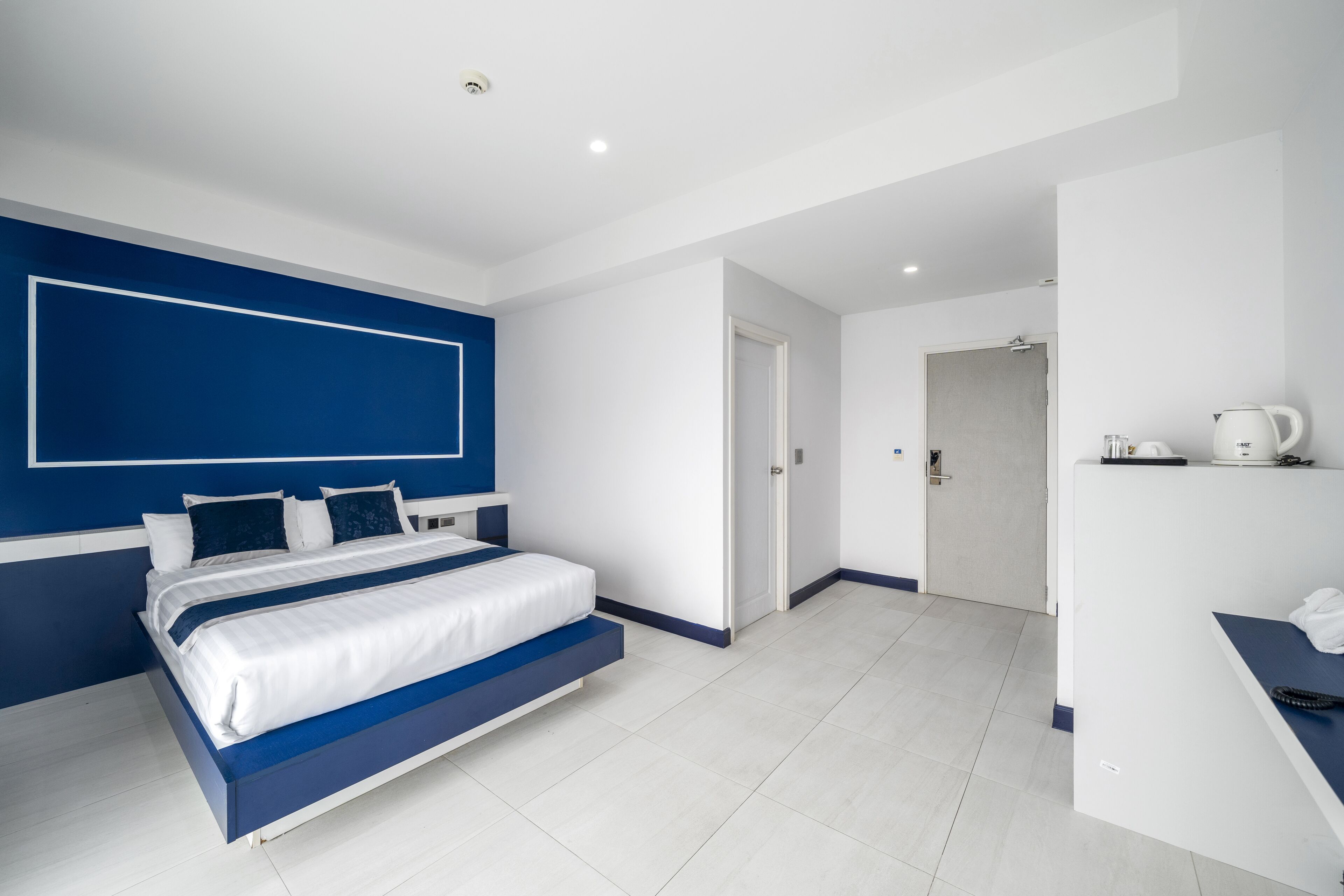 A modern hotel room with a large bed, a desk with a kettle, and a shower area.