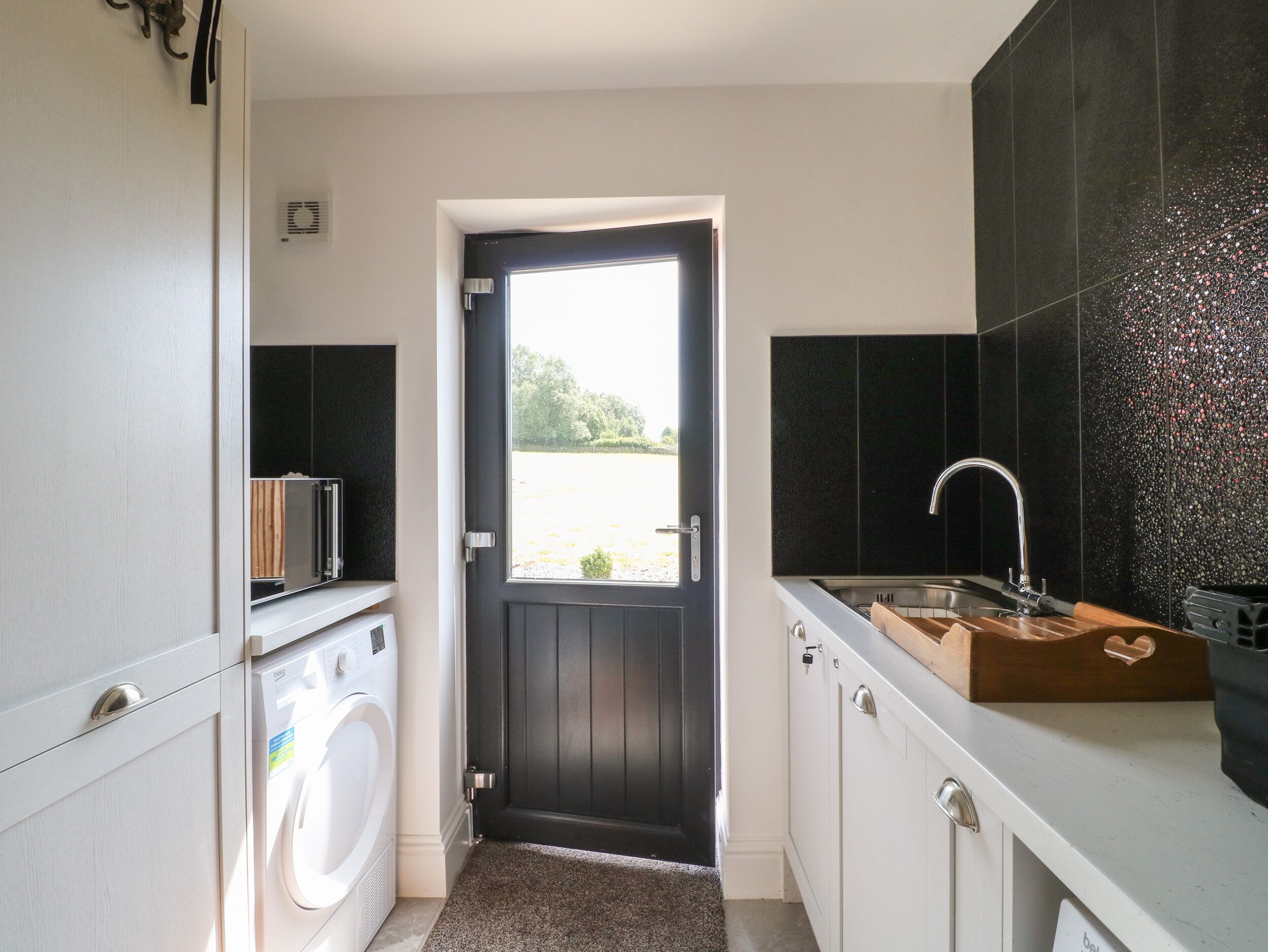 Cocina compacta con lavadora, un lavamanos y encimera de madera, y una puerta que da a un jardín.