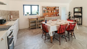 A dining area with a table set for four, a kitchen with modern appliances, and a bookshelf filled with books. - The Cottage (Chesterfield)