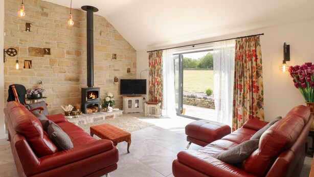 A living room with a stone wall, a fireplace, leather sofas, and a television. - The Cottage (Chesterfield)