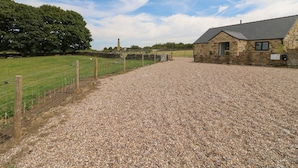 A gravel driveway leading to a stone building with a sloped roof, surrounded by a fenced field and trees. - The Cottage (Chesterfield)