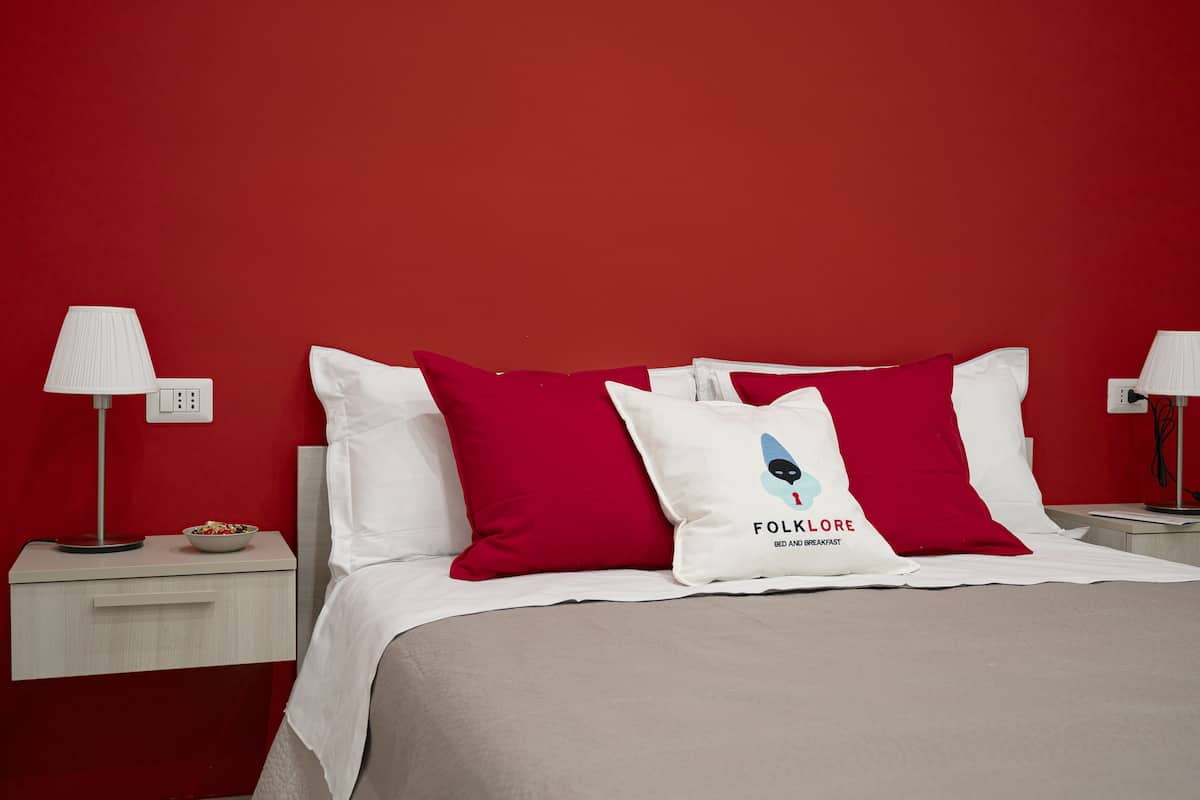 A hotel room with a red wall, a bed with white and red pillows, and bedside tables with lamps.