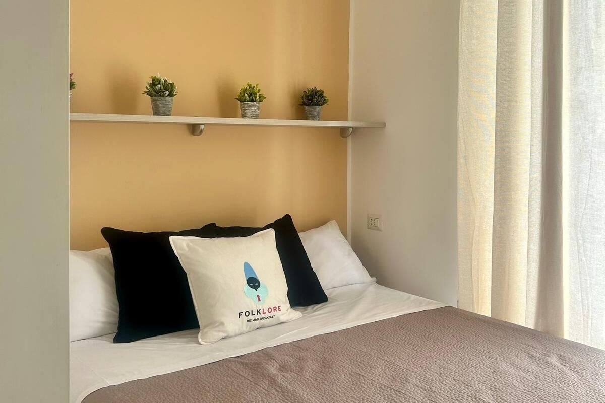 A neatly made bed with a white and brown bedspread, a pillow with a logo, and two small potted plants on a shelf above.