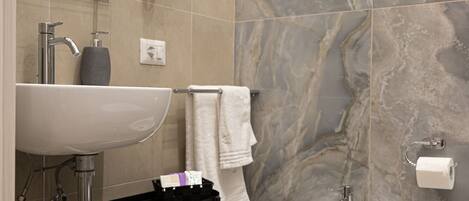 A modern bathroom with a marble backsplash, a white sink, a bidet, and a towel rack.