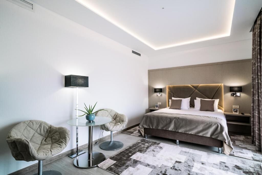 A modern hotel room with a large bed, two armchairs, a small round table, and a potted plant.