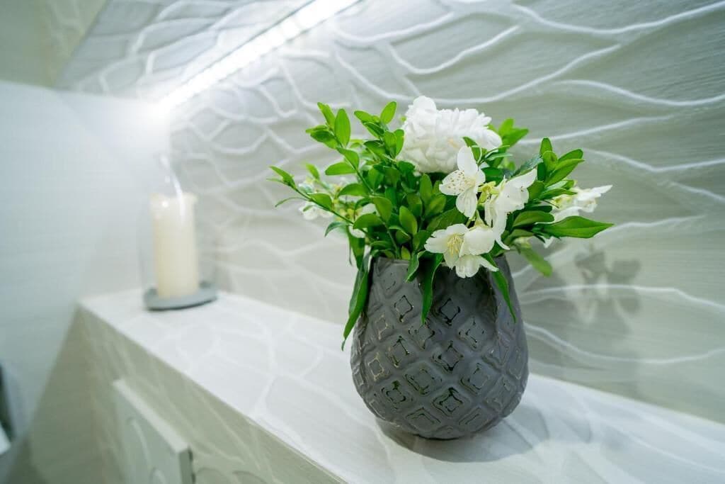 A vase with white flowers on a white shelf against a textured wall.