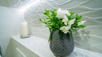 A vase with white flowers on a white shelf against a textured wall.
