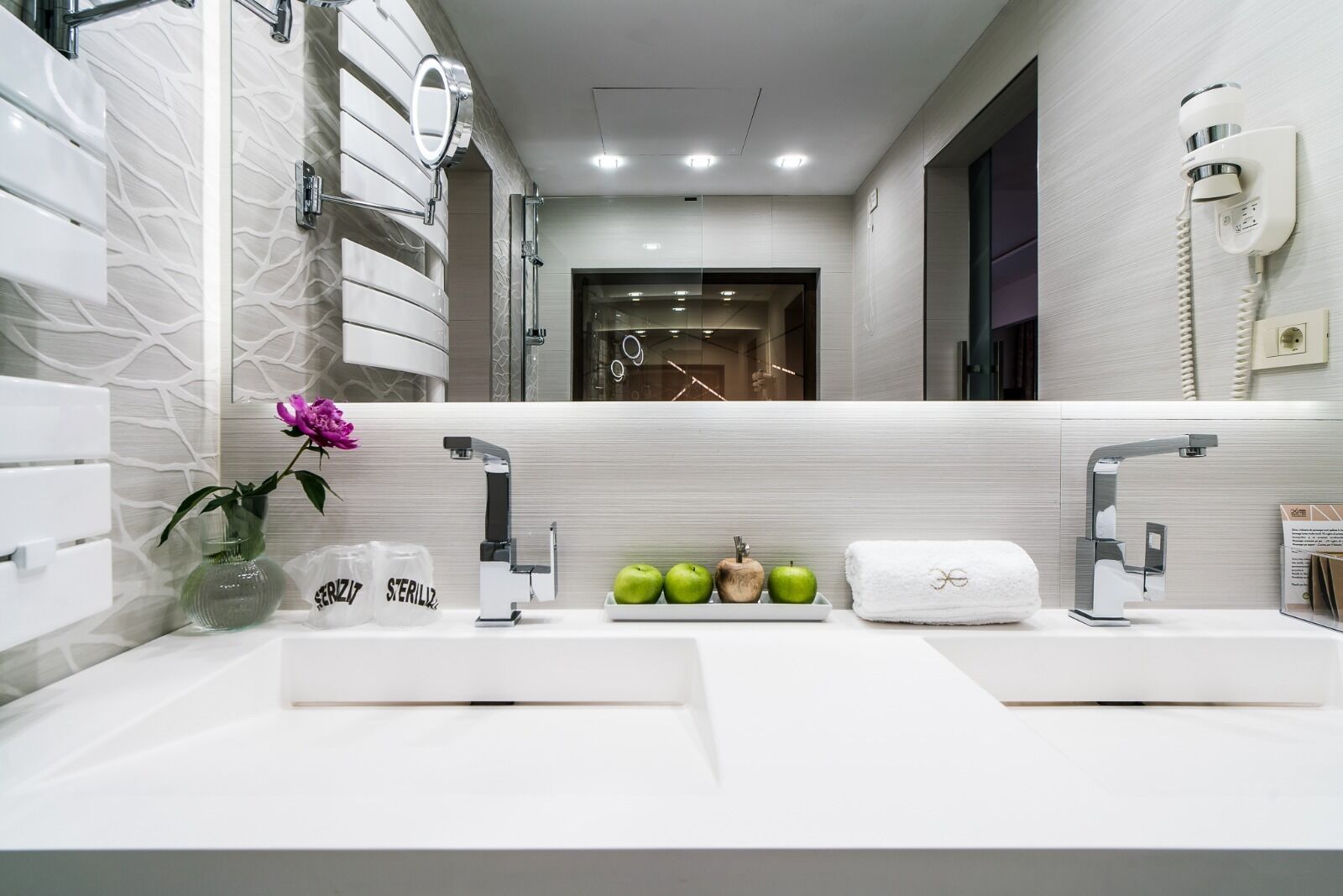A modern bathroom with two sinks, a vanity mirror, and a towel rack.
