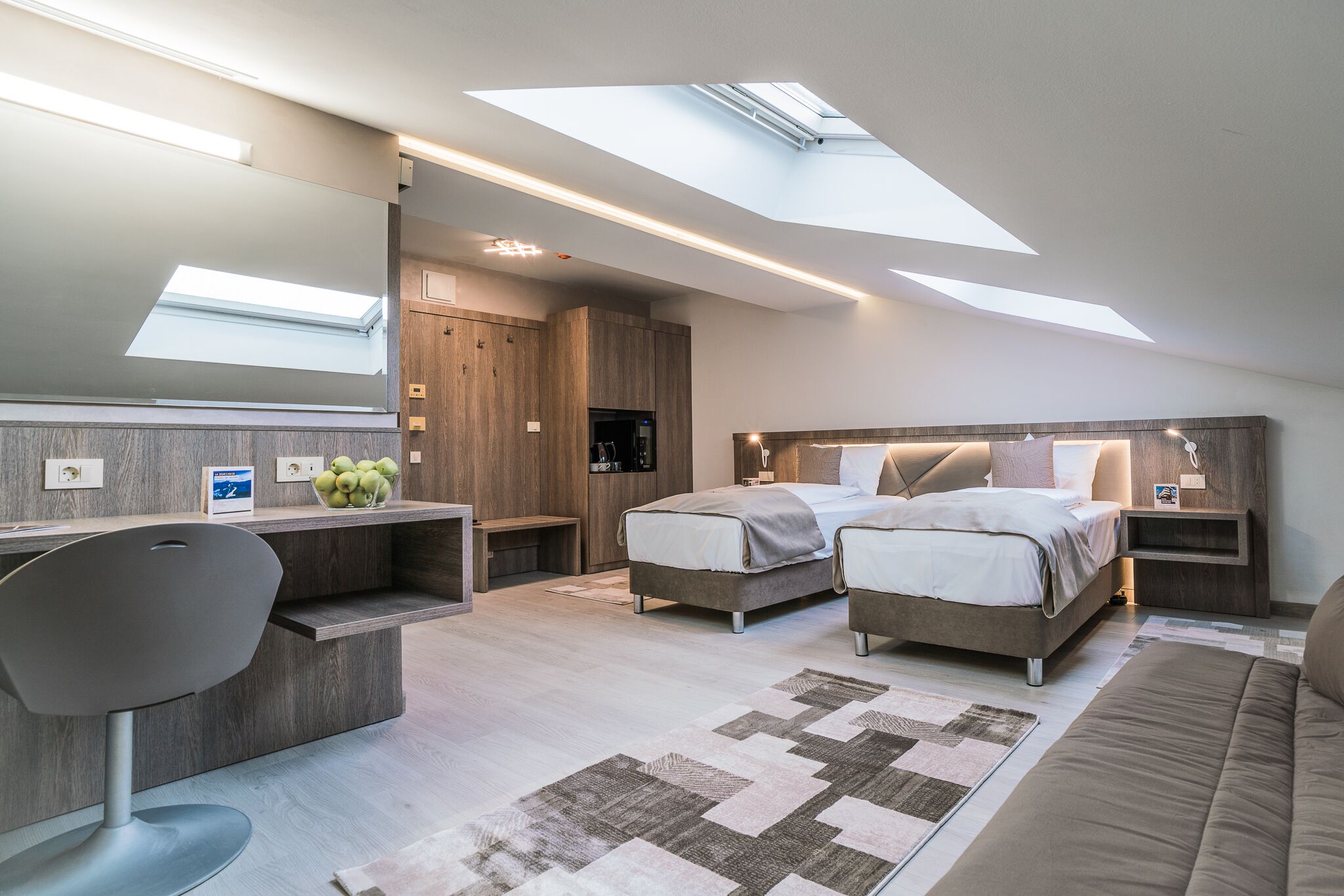 A modern bedroom with a skylight, two beds, a desk, and a couch.