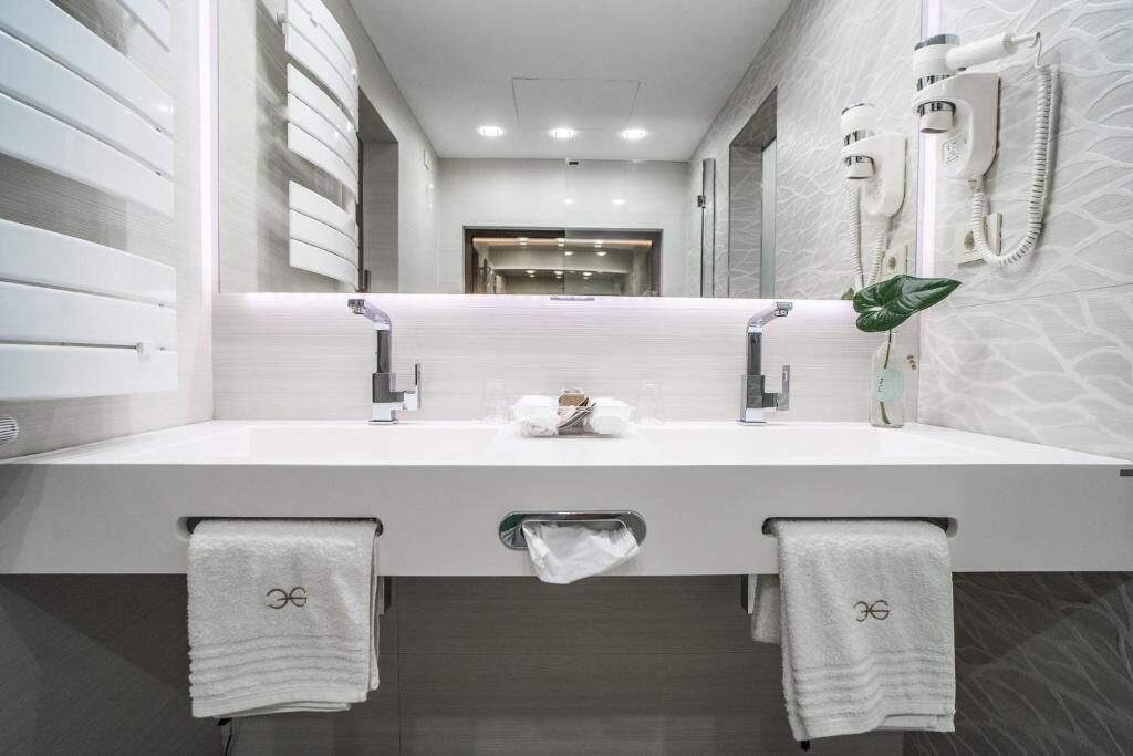 Un baño moderno con un lavamanos grande y blanco, dos toalleros, un espejo y una planta.
