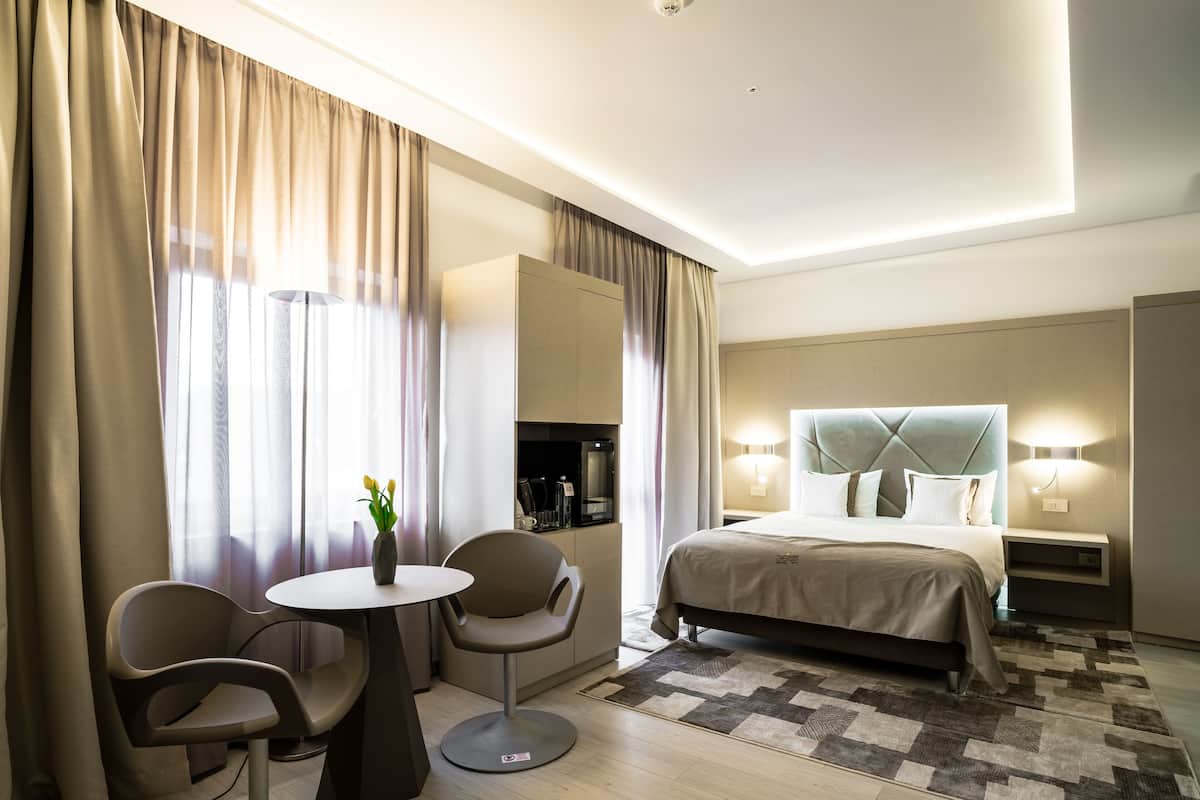 Una habitación de hotel moderna con una cama grande, una mesa redonda, dos sillas y un escritorio pequeño con una lámpara.