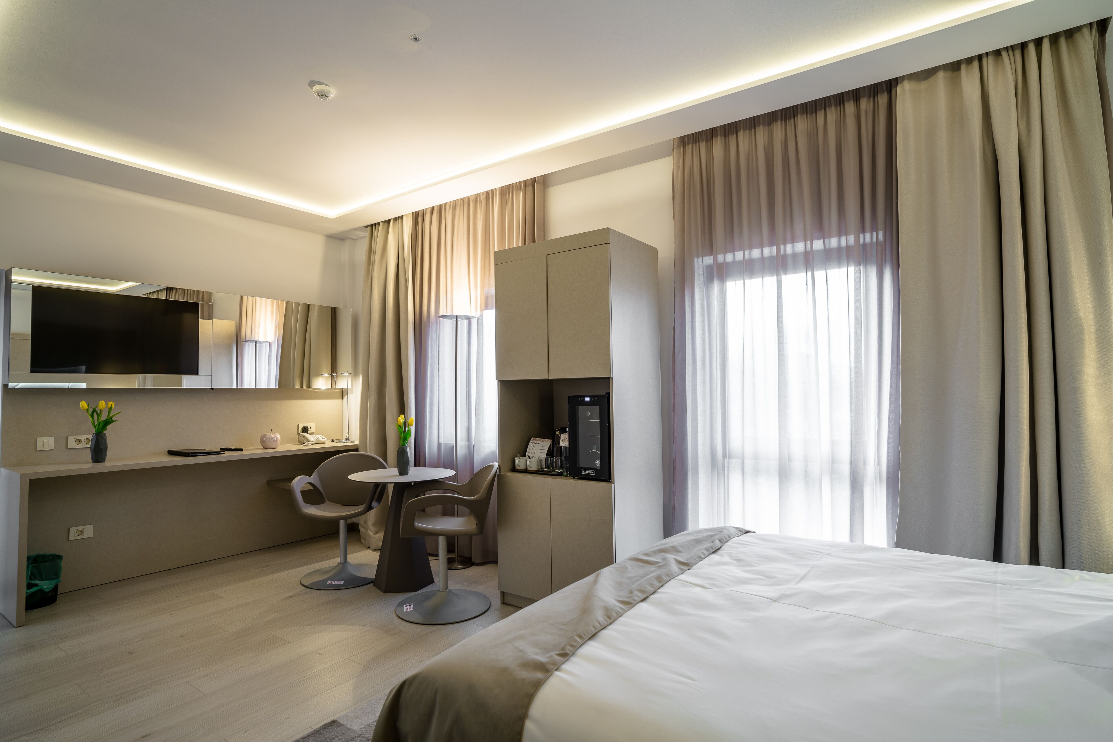 Une chambre d’hôtel moderne équipée d’un lit, d’un bureau avec une chaise, d’une télévision et d’un mini-bar.
