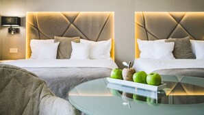Una habitación de hotel moderna con dos camas, una mesa redonda de cristal con un frutero y una lámpara de pared.
