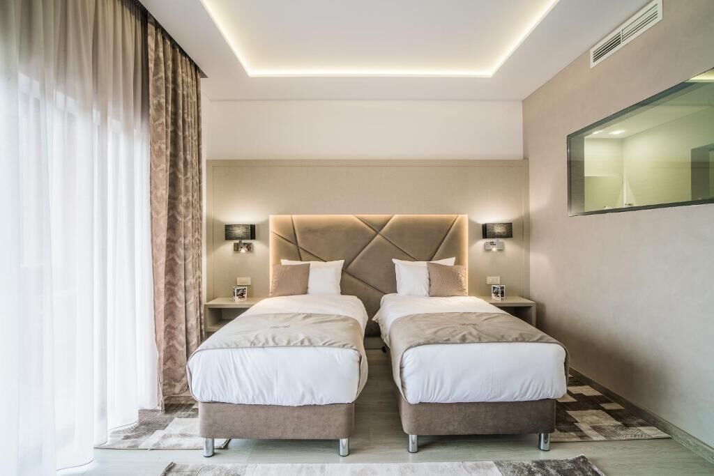 Ein modernes Hotelzimmer mit zwei Betten, einem großen Spiegel und einer Deckenleuchte.