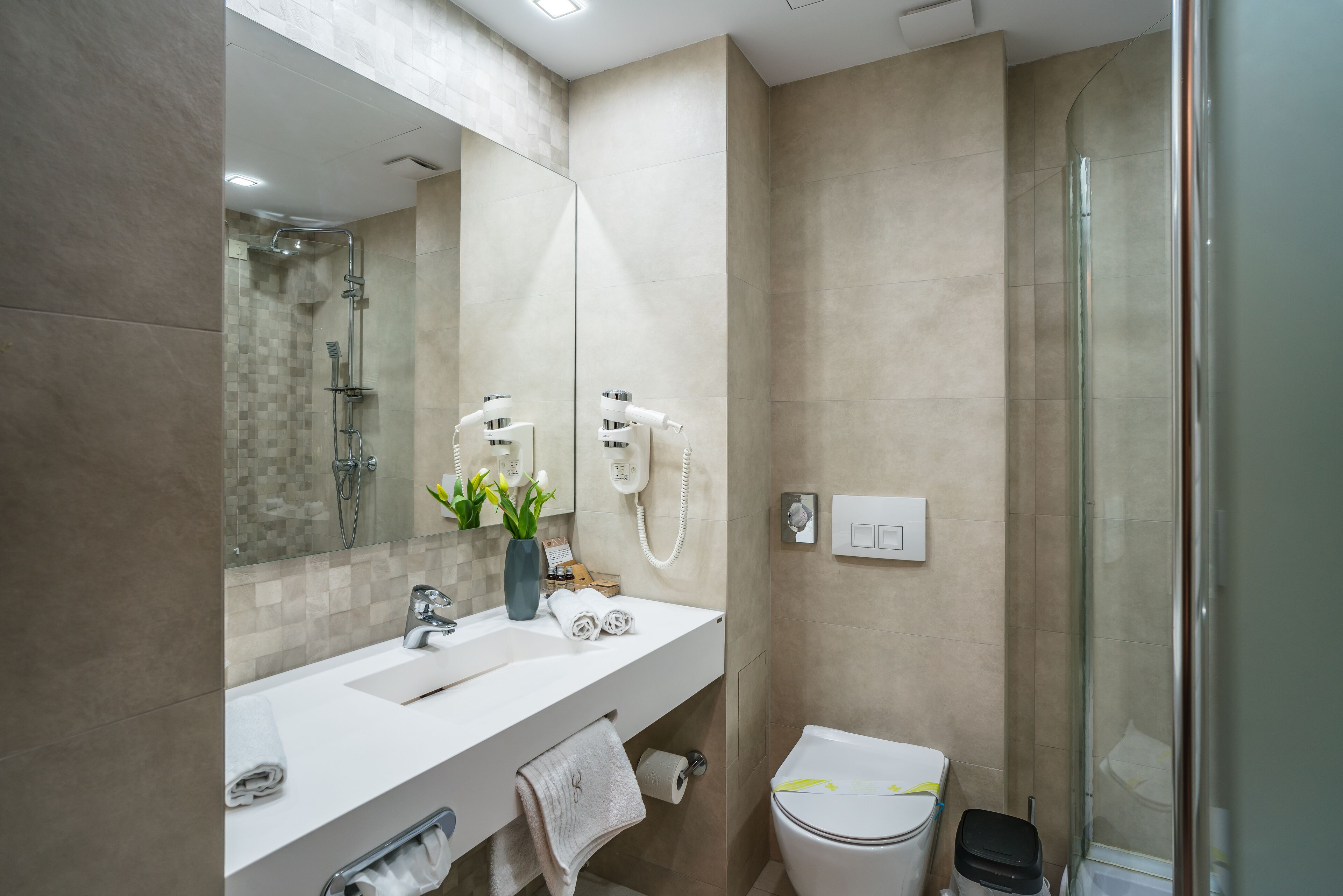 Een moderne badkamer met een grote spiegel, twee wasbakken, een toilet en een douchecabine.