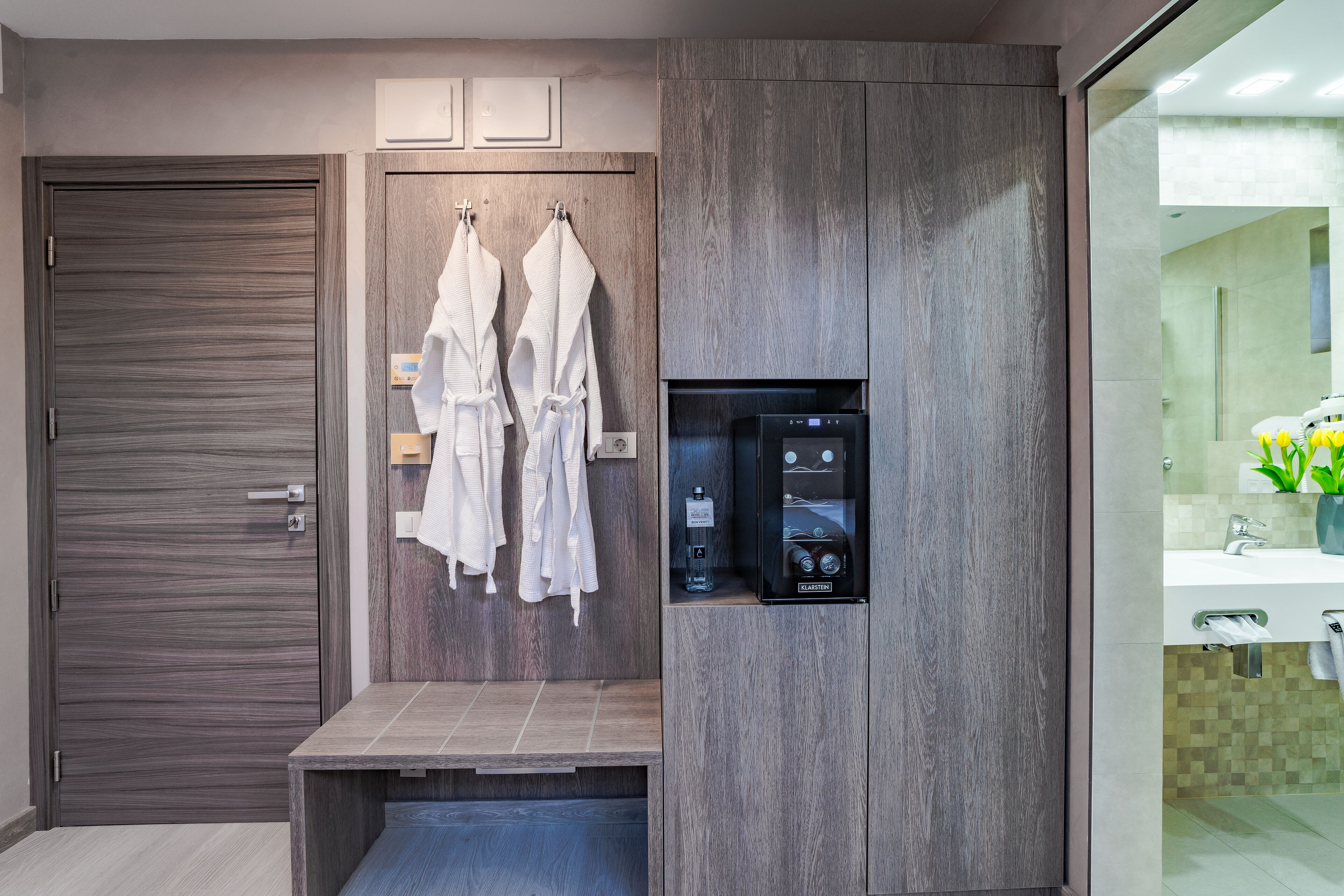 A modern bathroom with a wooden vanity, a built-in shower, and a towel rack with white robes.