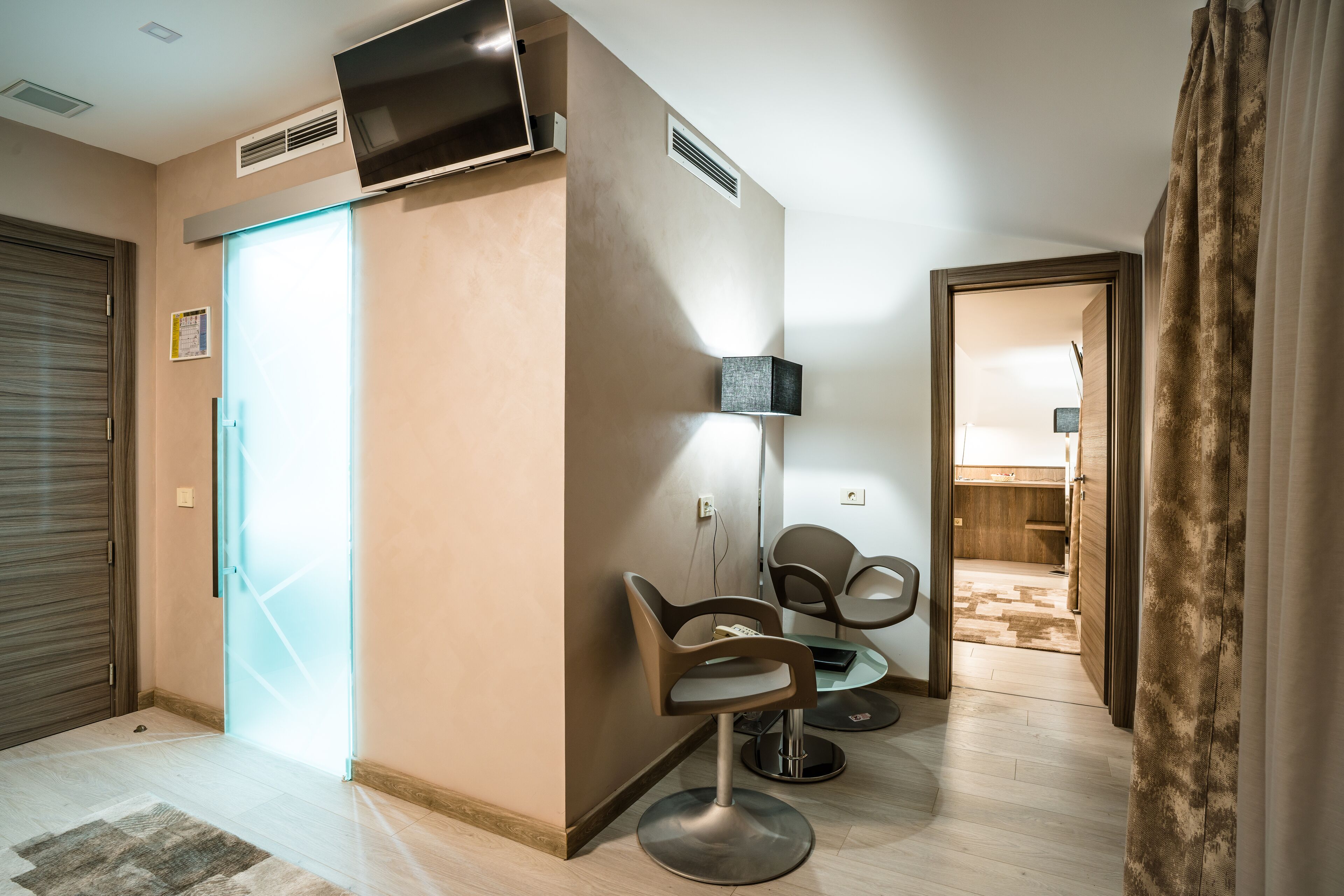 Ein modernes Interieur mit einer Sitzecke, einem an der Wand befestigten Fernseher und einem sichtbaren Badezimmer im Hintergrund.