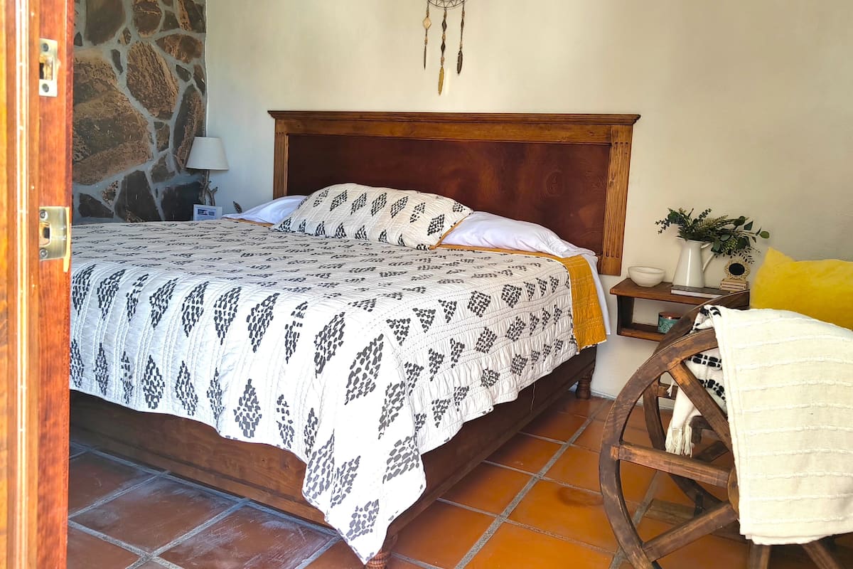 Un dormitorio con cama de madera, pared de piedra y un atrapasueños colgado.