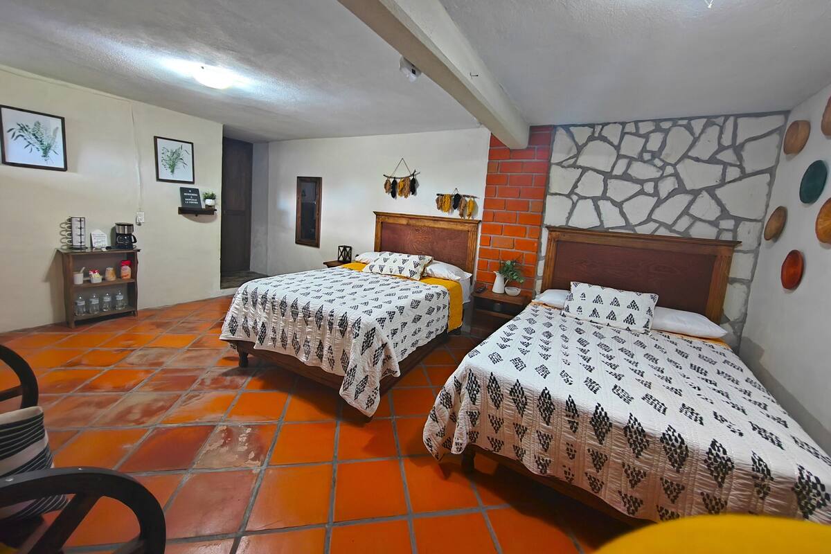 Habitación de hotel con dos camas, una cafetera, una mesita y una pared de ladrillo.