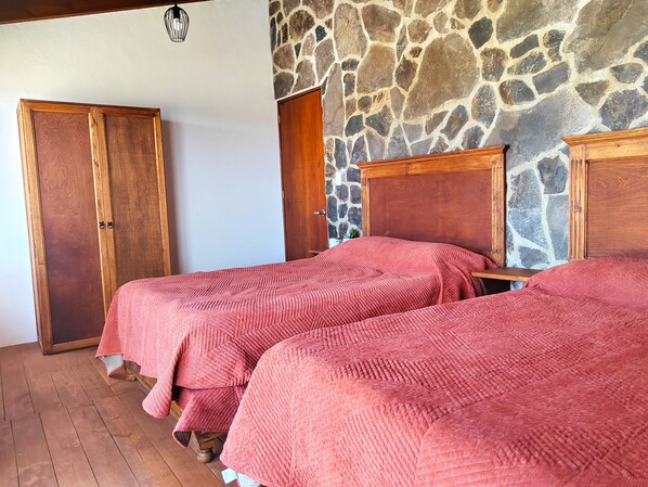 A room with two wooden beds, a stone wall, and a wooden wardrobe.
