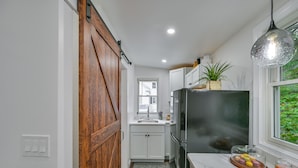 A kitchen with white cabinets, a black refrigerator, a wooden door, and a window with a view of greenery. - 5 Mi to Salem: Furnished Patio at Danvers Studio! (Danvers)