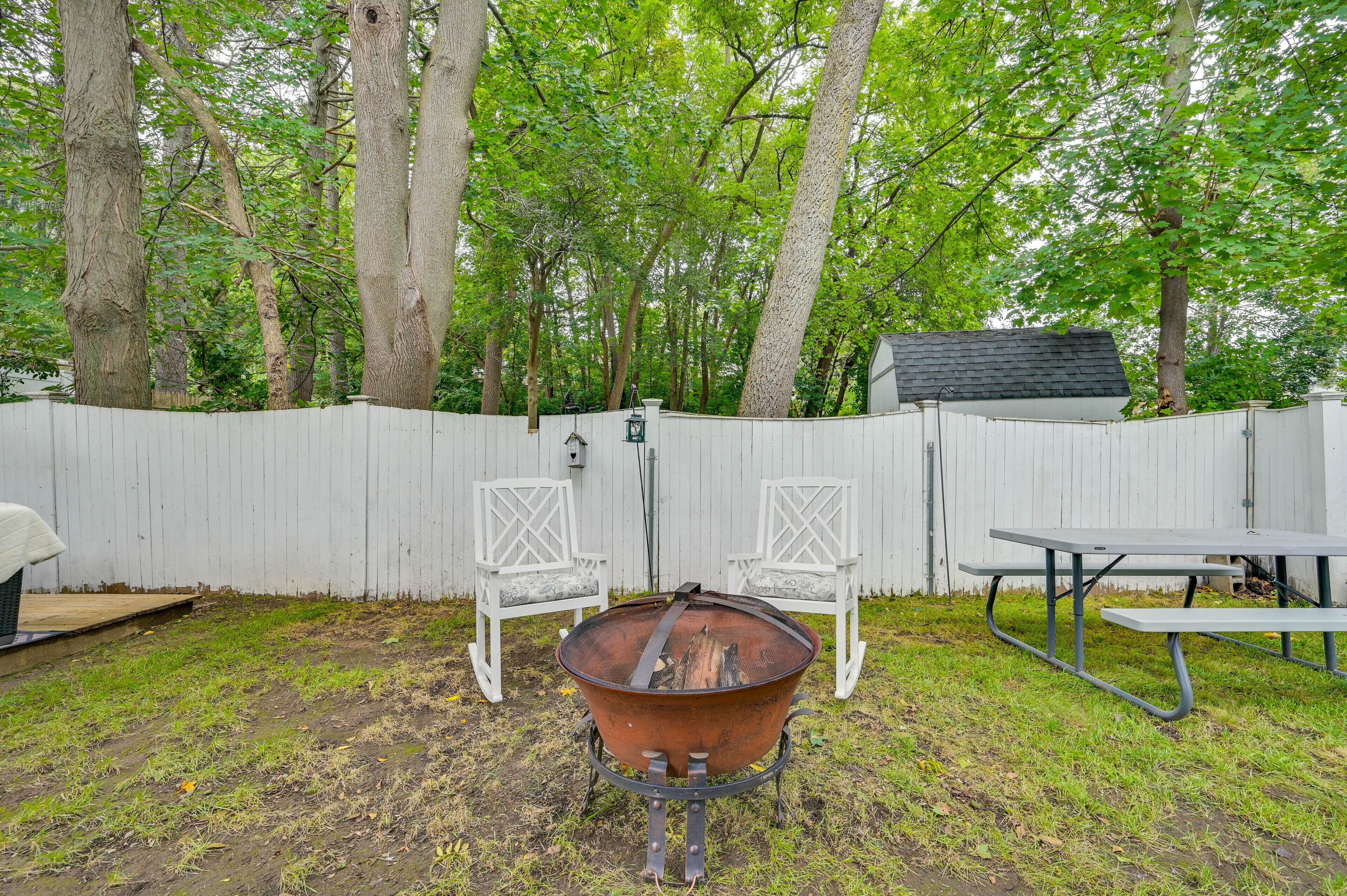 Un jardin avec un foyer, deux chaises blanches et une table de pique-nique.