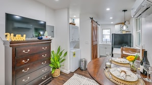 A modern kitchen with a TV, wooden cabinets, a dining area with a table set for two, and a sliding door leading to another room. - 5 Mi to Salem: Furnished Patio at Danvers Studio! (Danvers)